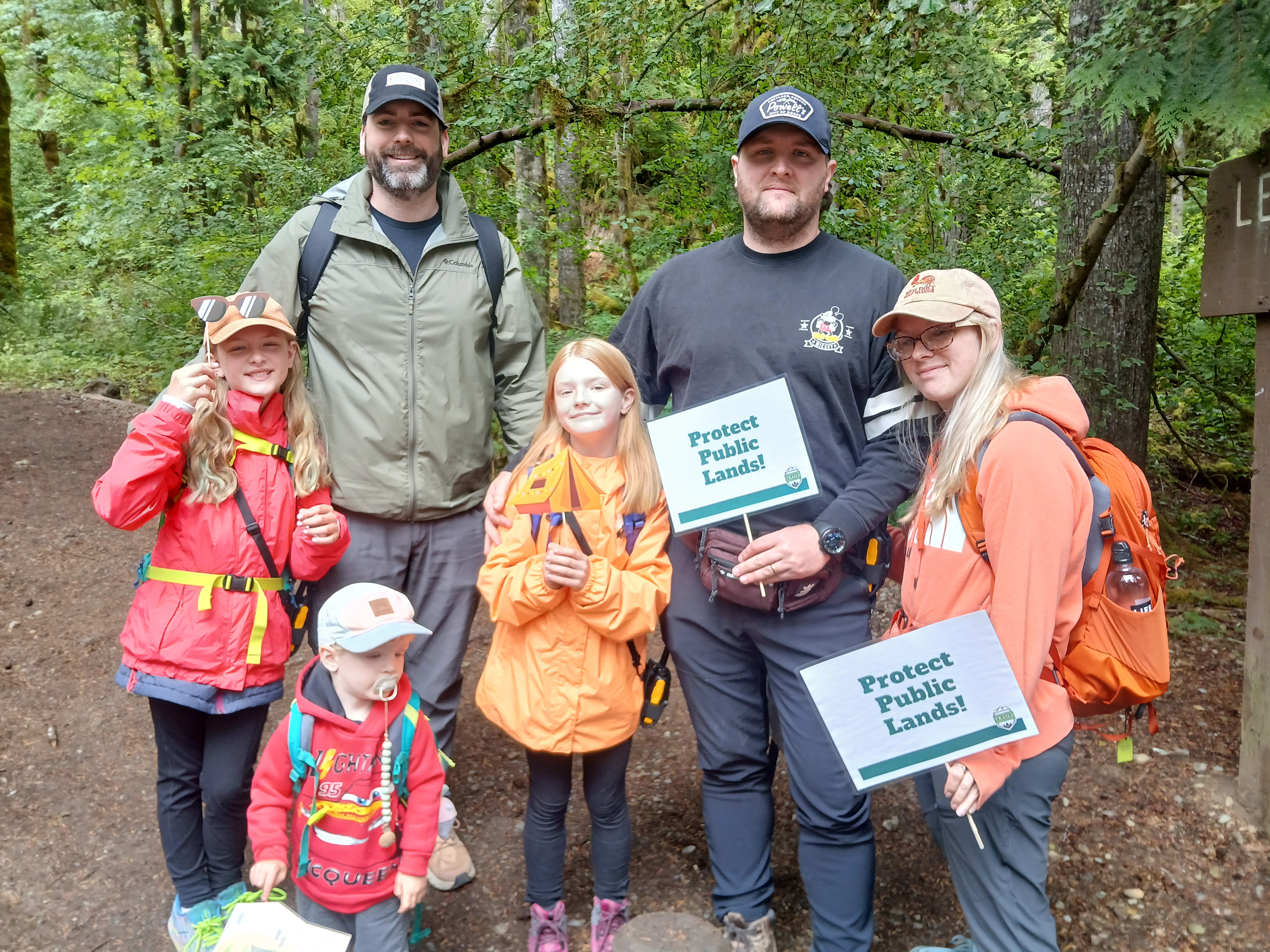 Family of adults, two children and a toddler hold signs saying, "Protect public lands!"
