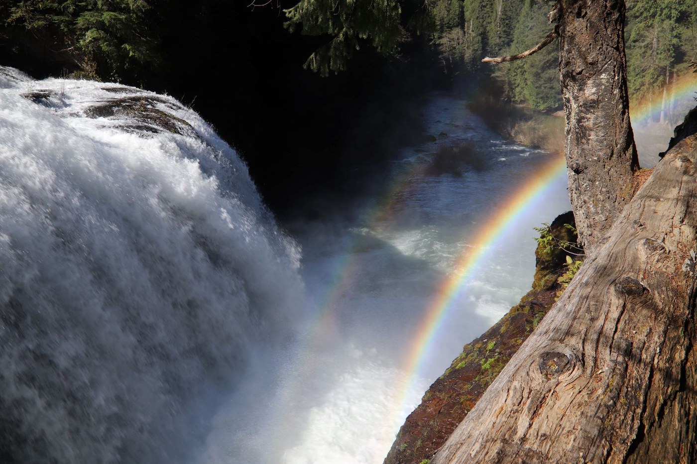 A wide waterfall pours down into a valley, creating a rainbow
