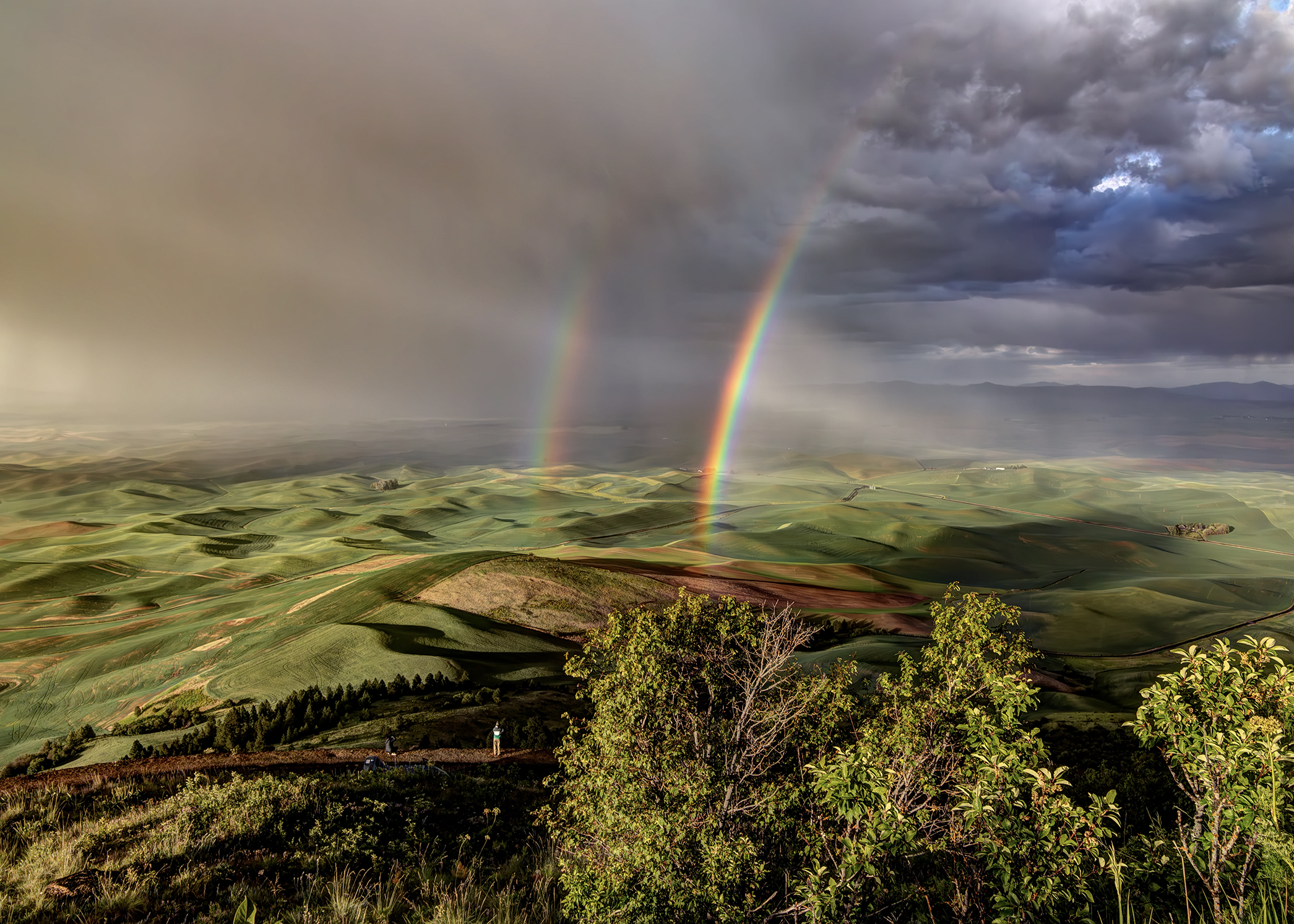A double rainbow over rolling, shadowed green hills