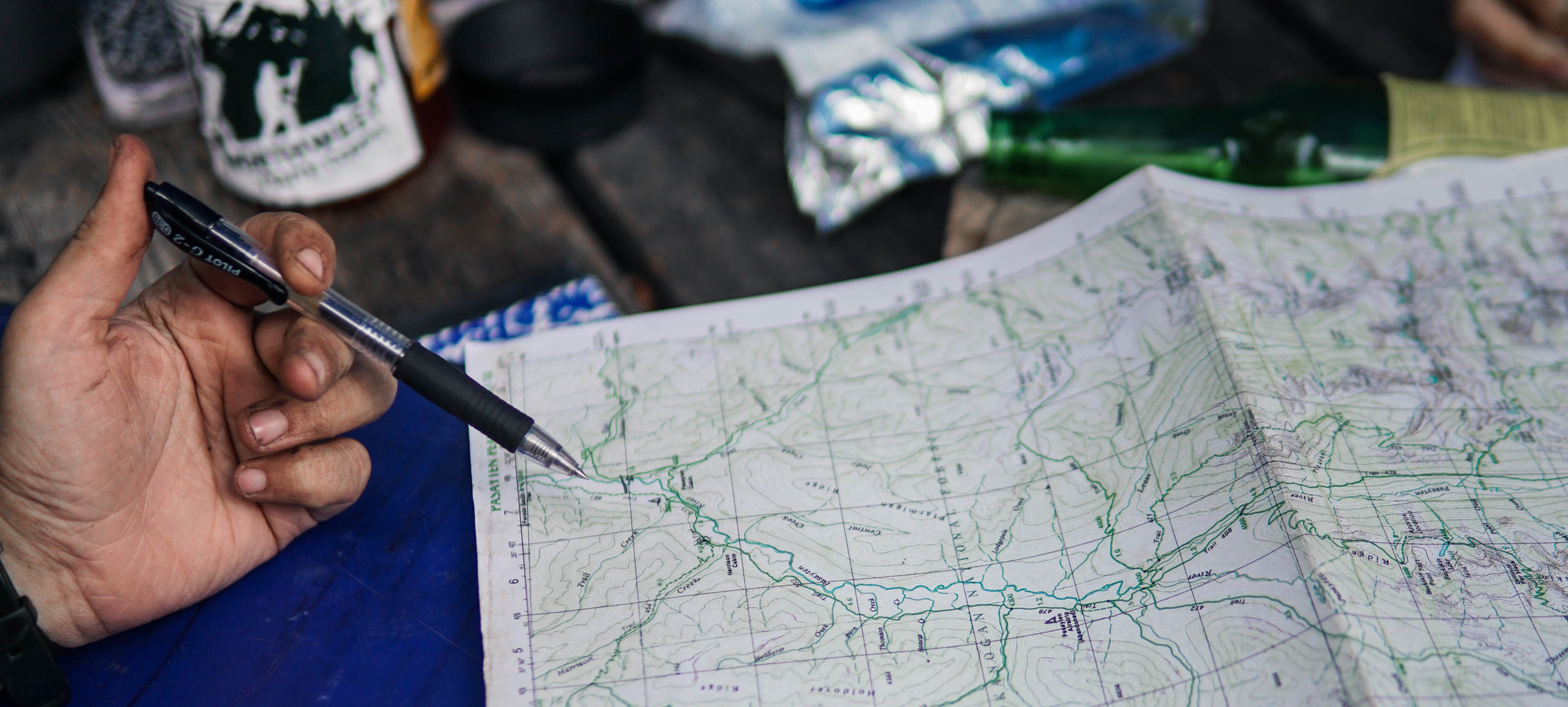 A hand with a pen over some paper topographical maps. Photo from WTA archives.