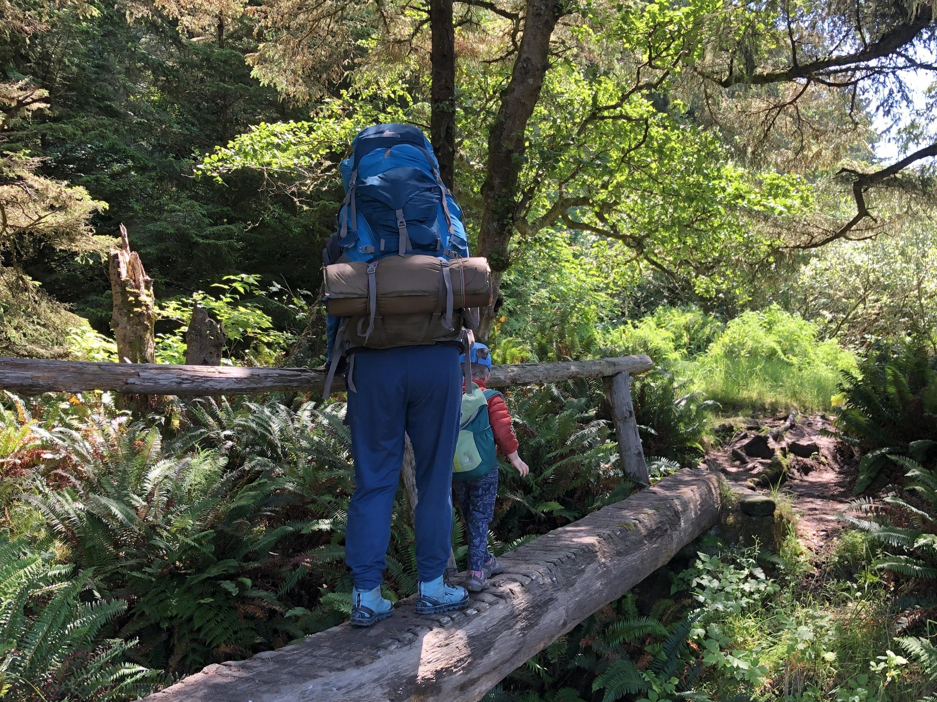 Backpacking with kiddos. Photo by Loren Drummond. An adult with a backpacking pack on guides a child over a bridge. Photo by Loren Drummond.