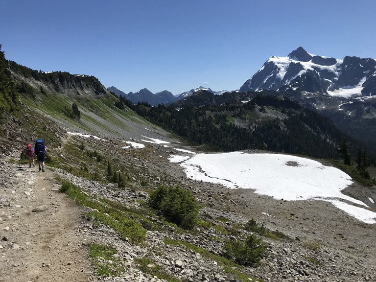 Two kids head into the Chain Lakes area at Mount Baker with craggy Mount Shuksan on the horizon. 