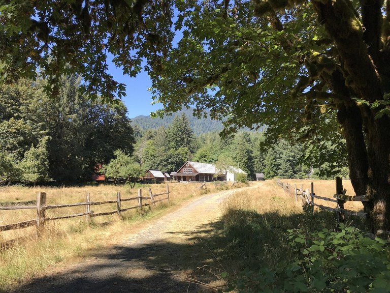 A dirt road parallels an old wooden fence with an old farm building in the distance. Photo by somewhat slow Susan