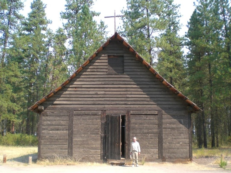 A man stands in front of an old A-frame building. Photo by Holly Weiler. 