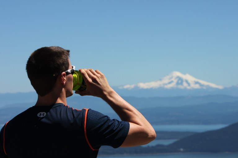 Hiker with mountain in backdrop drinking water.