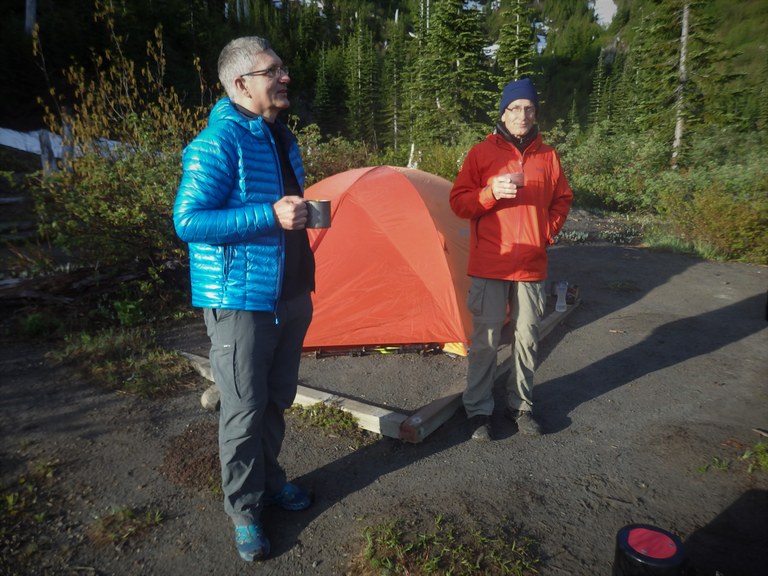 Two campers drinking coffee by their tent in the morning.