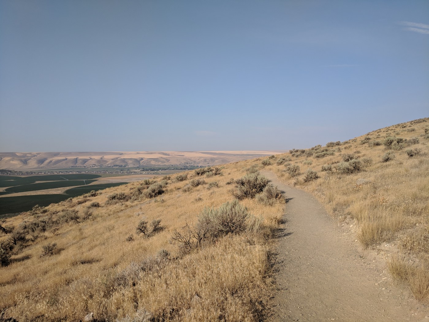 Badger Trail along dry grassy hills with a view to a distant town in the valley. Photo by Luffles.