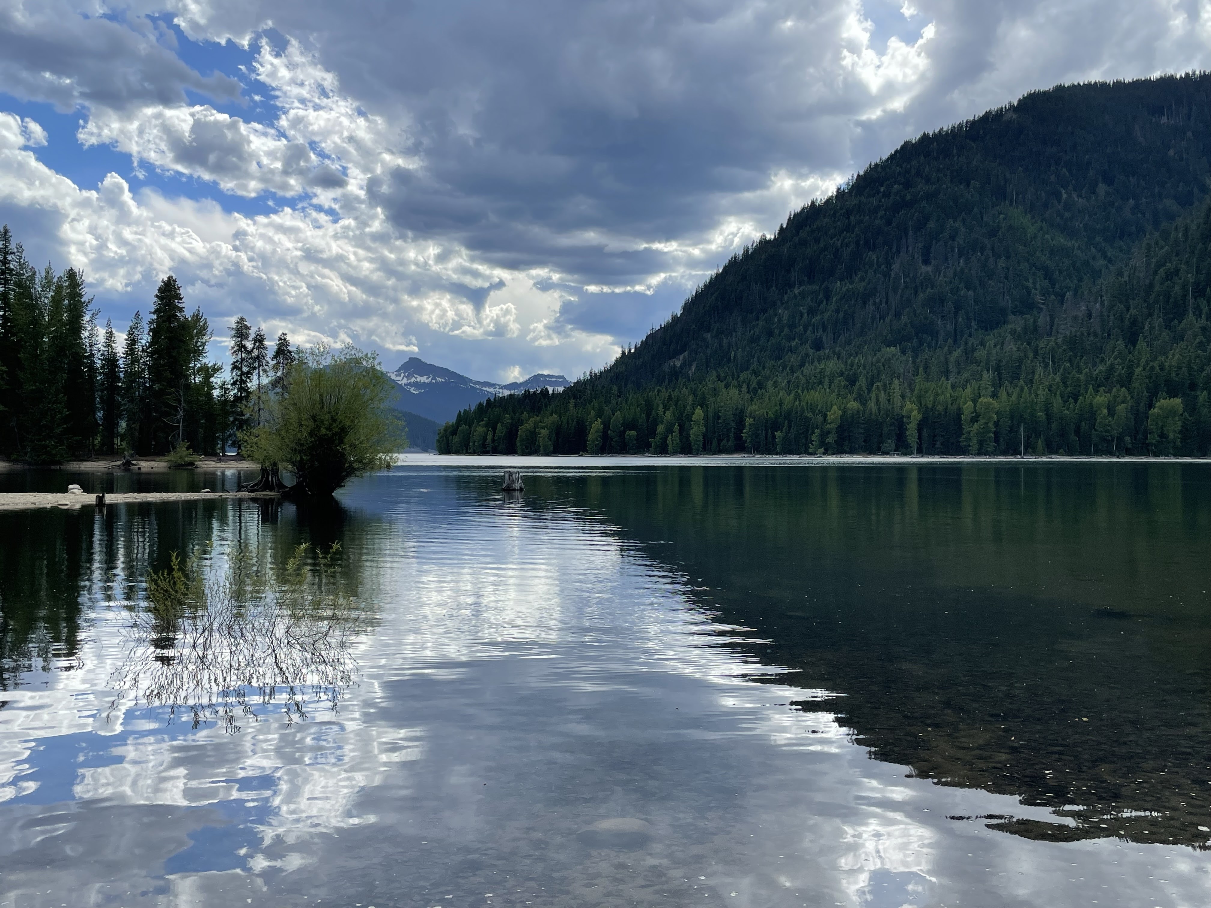 Still, quiet lake sits below a sky full of clouds and a dark green hillside