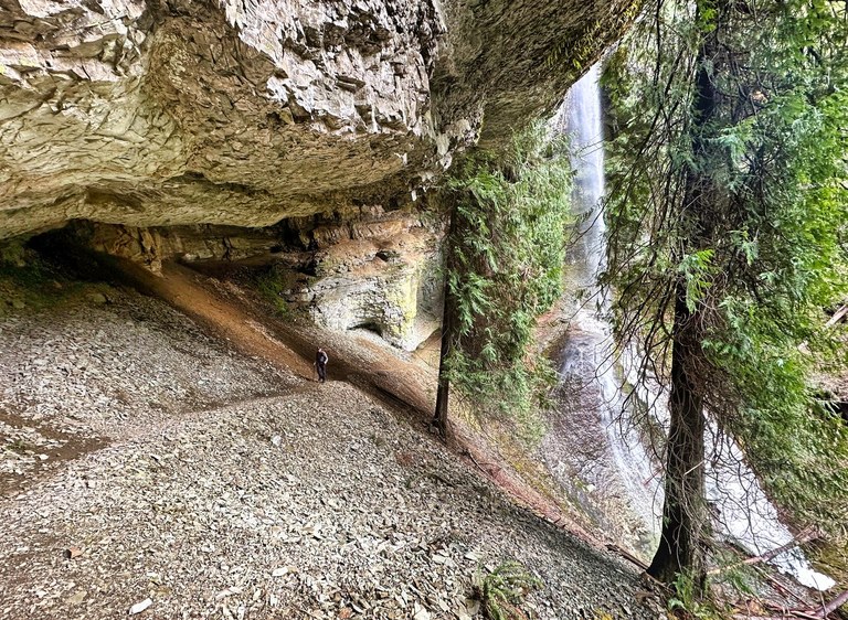 A hiker continues on a somewhat exposed trail behind a waterfall.