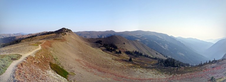 An expansive panorama of a fall-color strewn ridgeline with mountains in the distance.