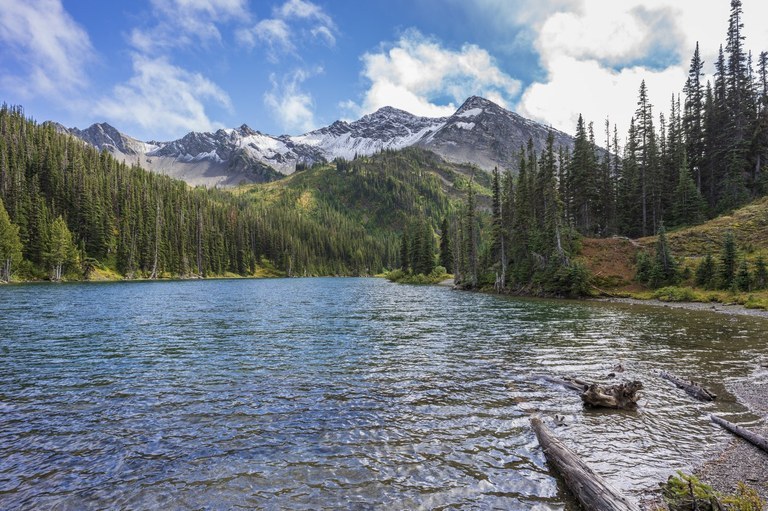 Snowy mountain peaks and evergreen trees circle a blue lake.