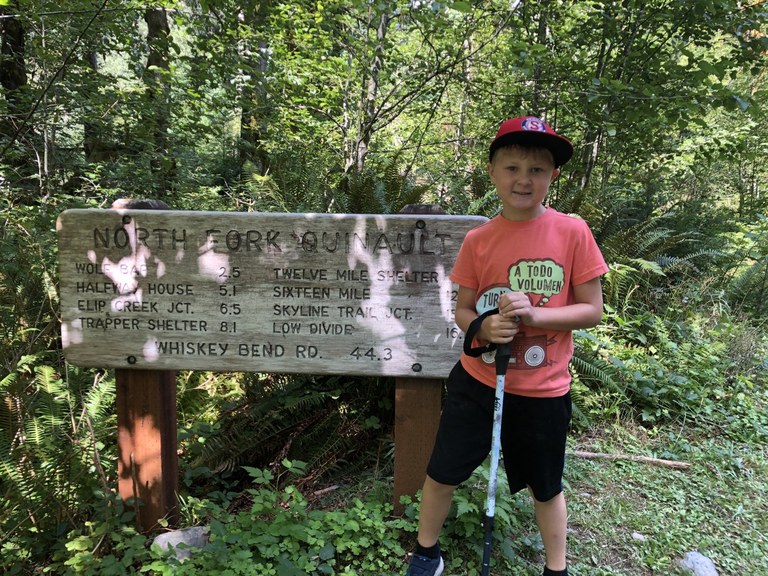 A young child in an orange t shirt stands at the trailhead for the North Fork.