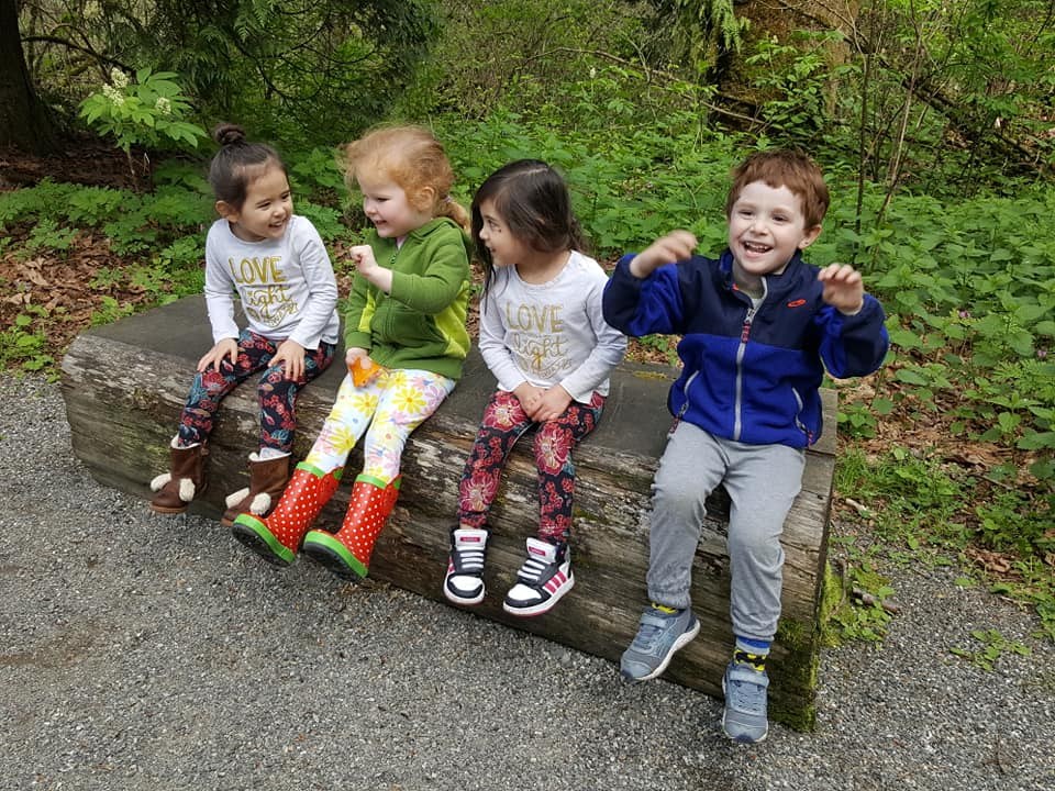 Four smiling little kids sit on a wooden bench. 