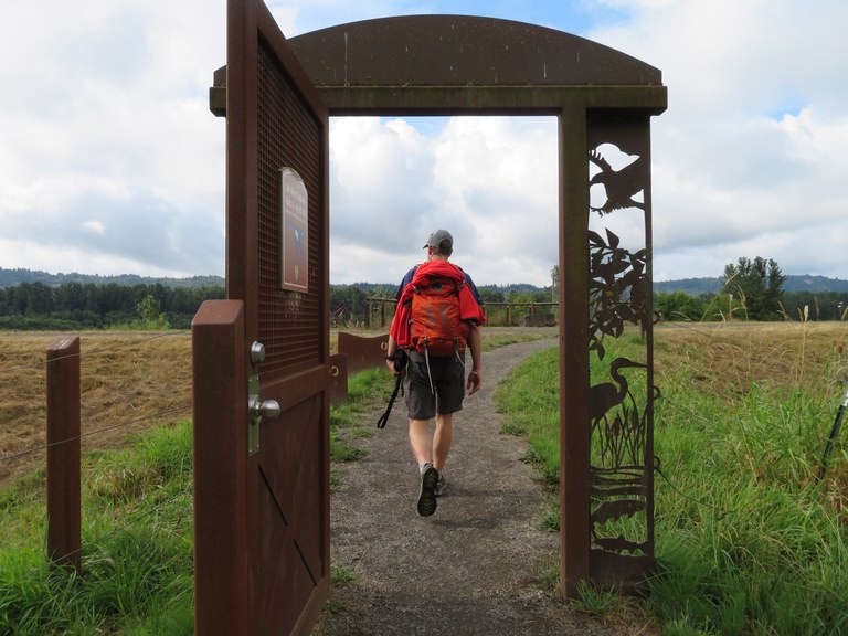 A man walks through a metal arch to enter an open grass field. 