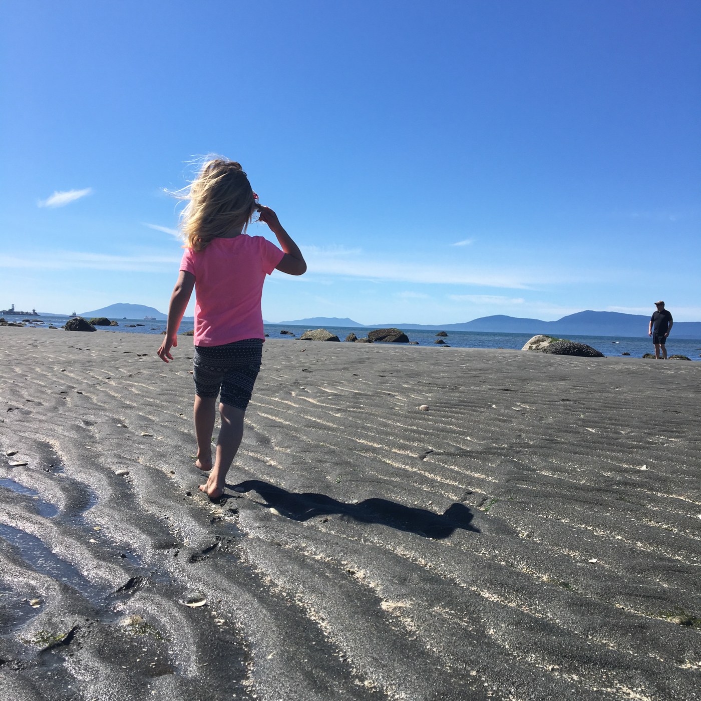 A kid walks on a sandy beach under bright sun. 