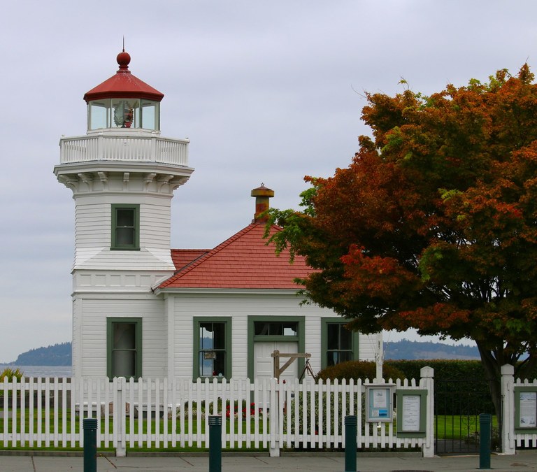 A lighthouse with a tree with leaves changing from green to red. 