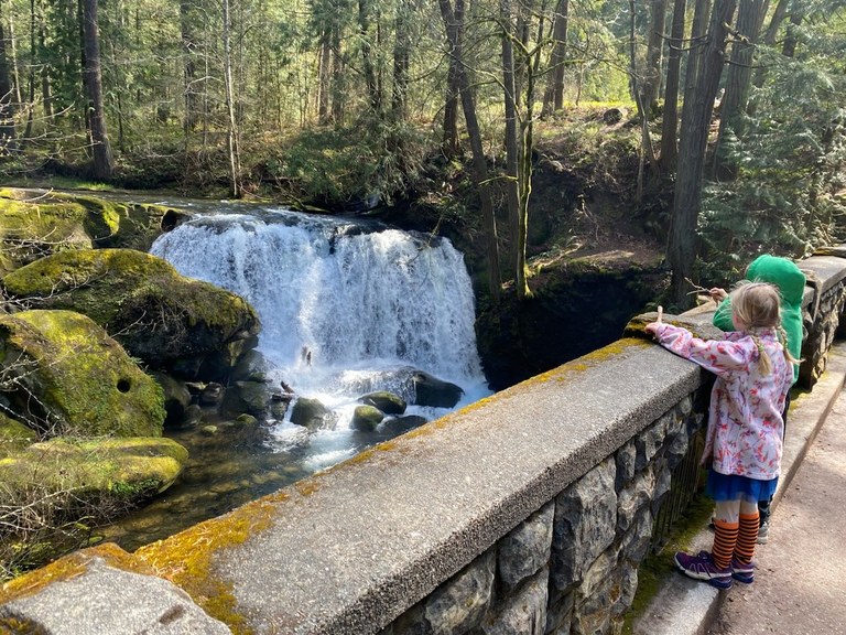 Two small kids stand o the stone bridge over the Whatcom Falls Bridge