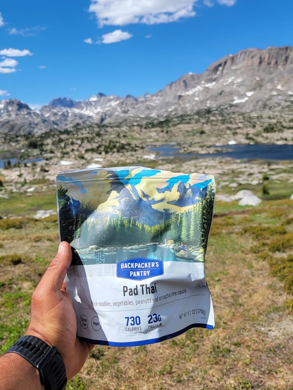 A dehydrated meal is held in front of a backdrop of mountains.