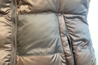 A close-up on a gray down jacket with a patch near the left pocket.