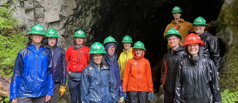 A group of several volunteers stand in front of a tunnel wearing rain coats