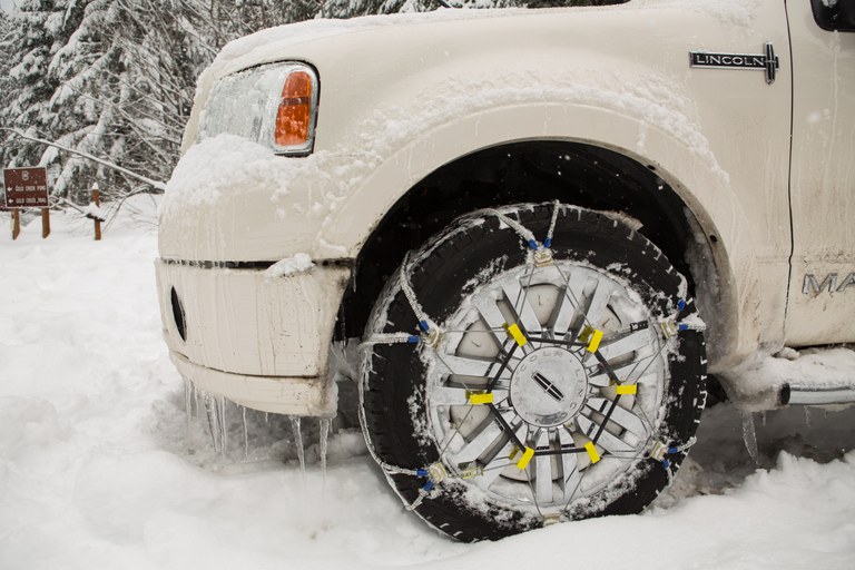 An SUV is parked alongside a snow road with chains on the tires. 