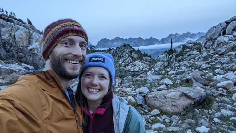 The author and her partner smile for a photo with mountains in the background in the evening light.