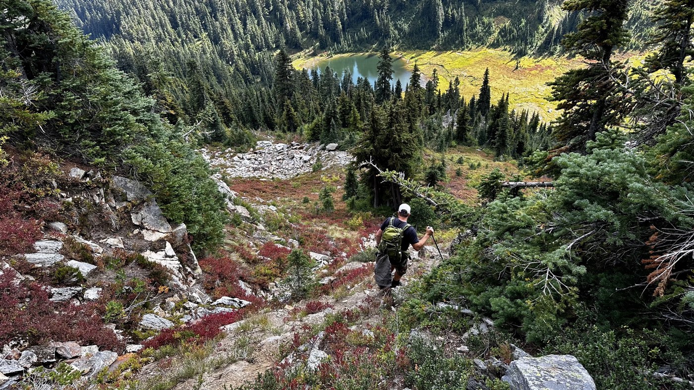 Hiker with a pole makes their way down a steep, rocky path towards a lake