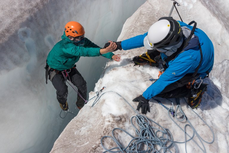 A climber helps another climber out of a crevasse. 