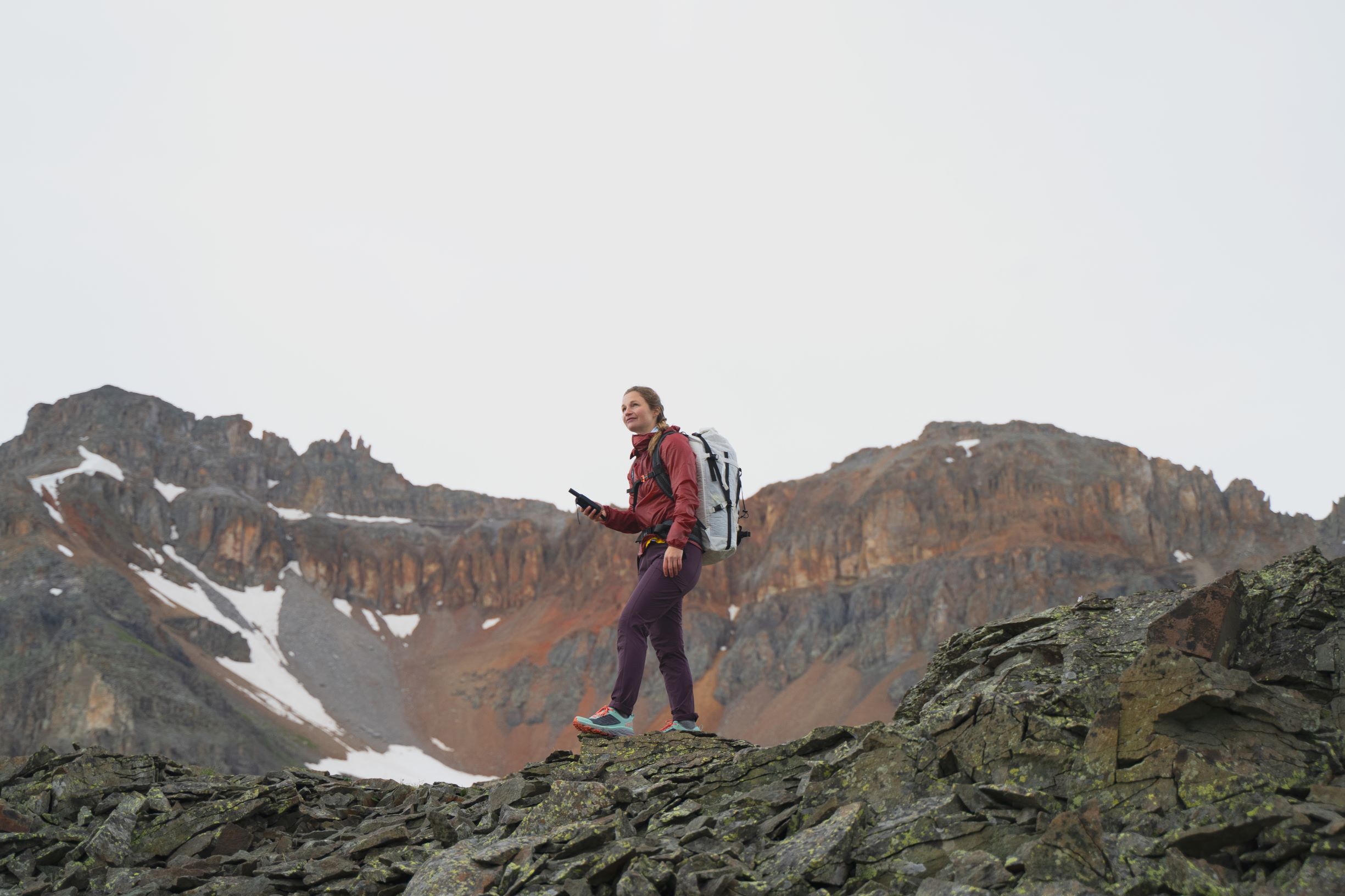 A hiker stands calmly holding a SPOT device in their hand and overlooking a rocky hillside.