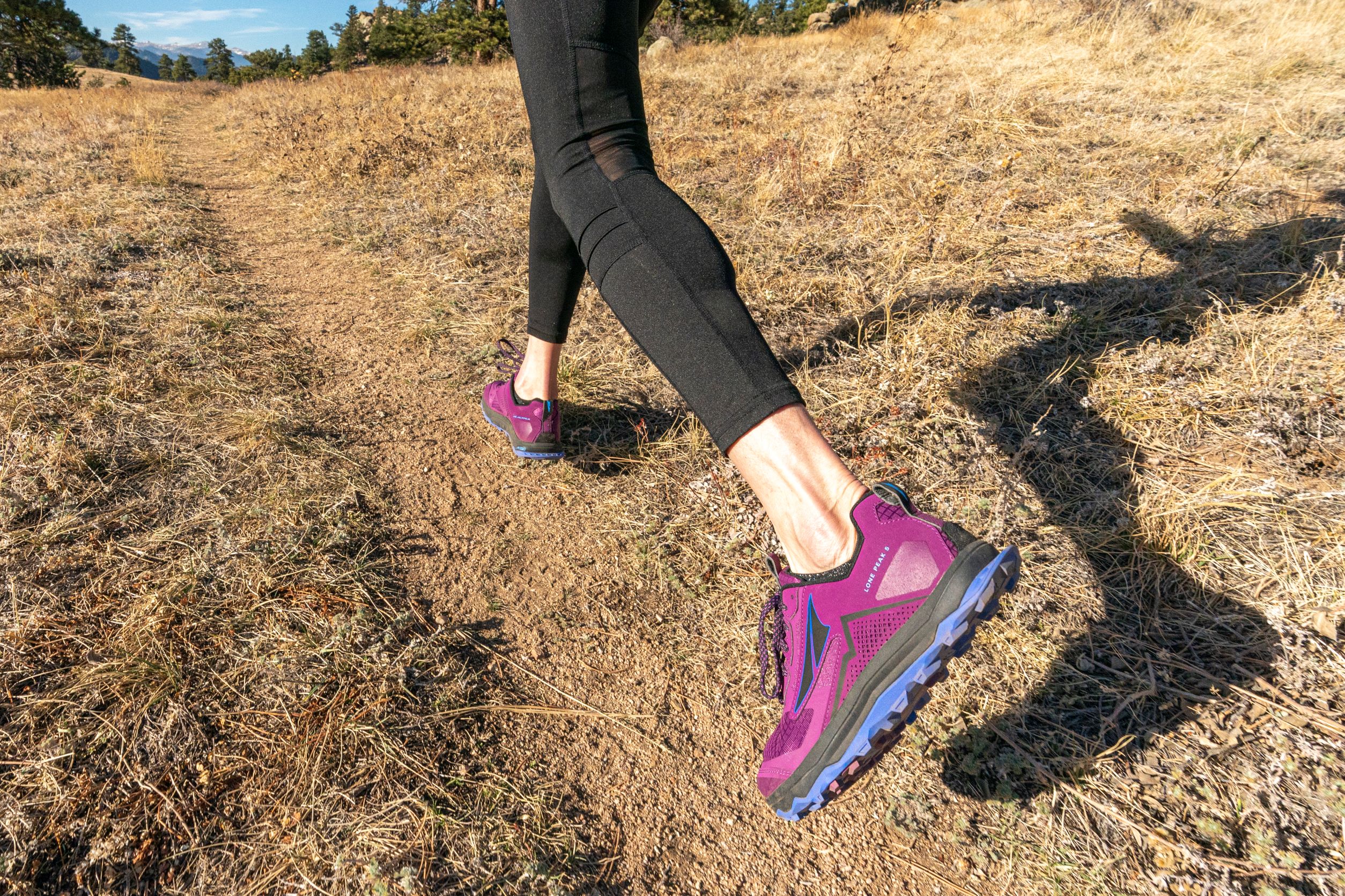Altra Lone Peaks are a favorite for many hikers. A hiker in leggings and Altra Lone Peaks runs down a dirt trail.