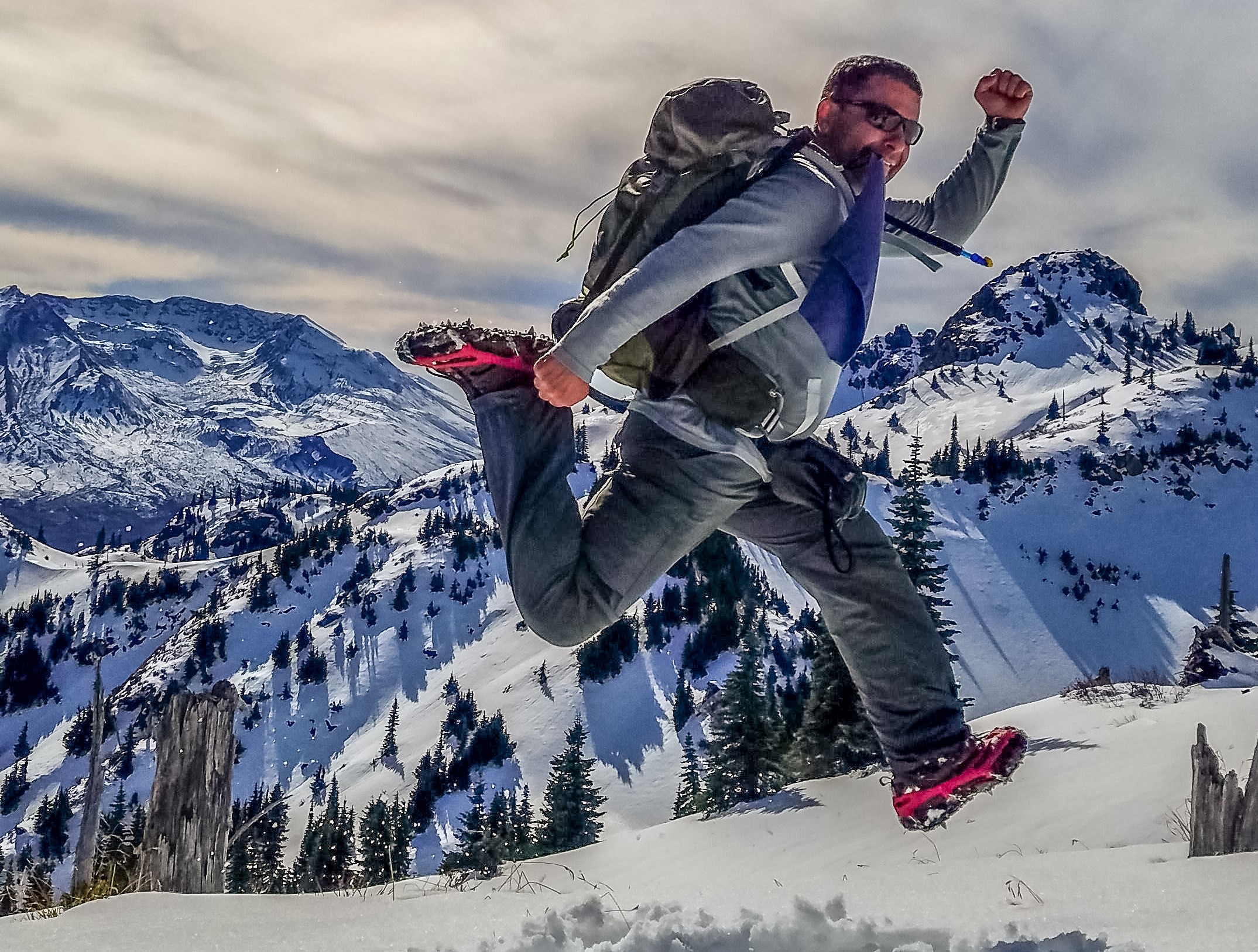 A hiker leaps up in the snow to show off their over-the-shoe traction aid.