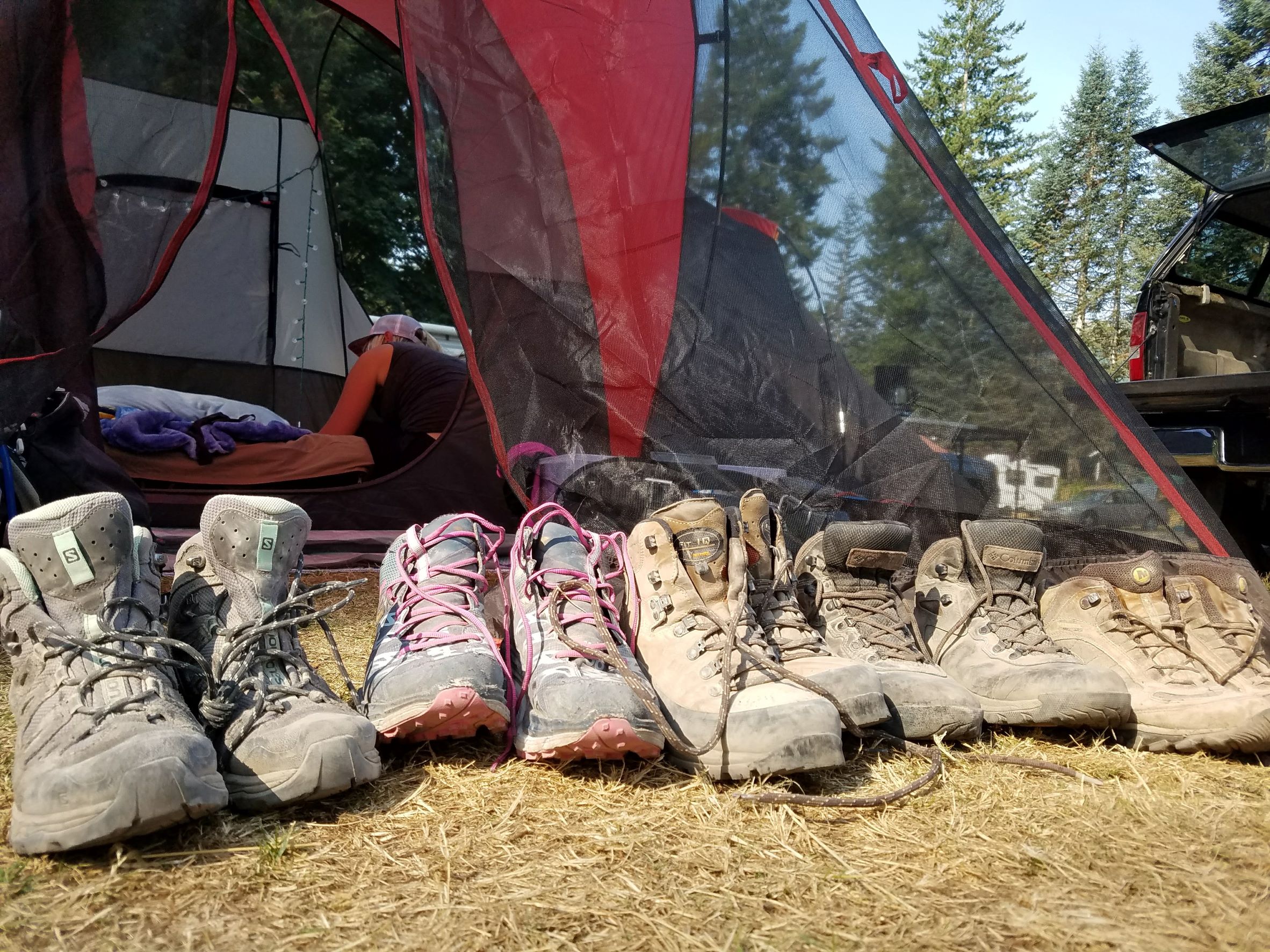 Giving your hiking shoes time to dry out is key for their longterm durability. A row of dusty hiking boots sit out in the sun in front of a tent.