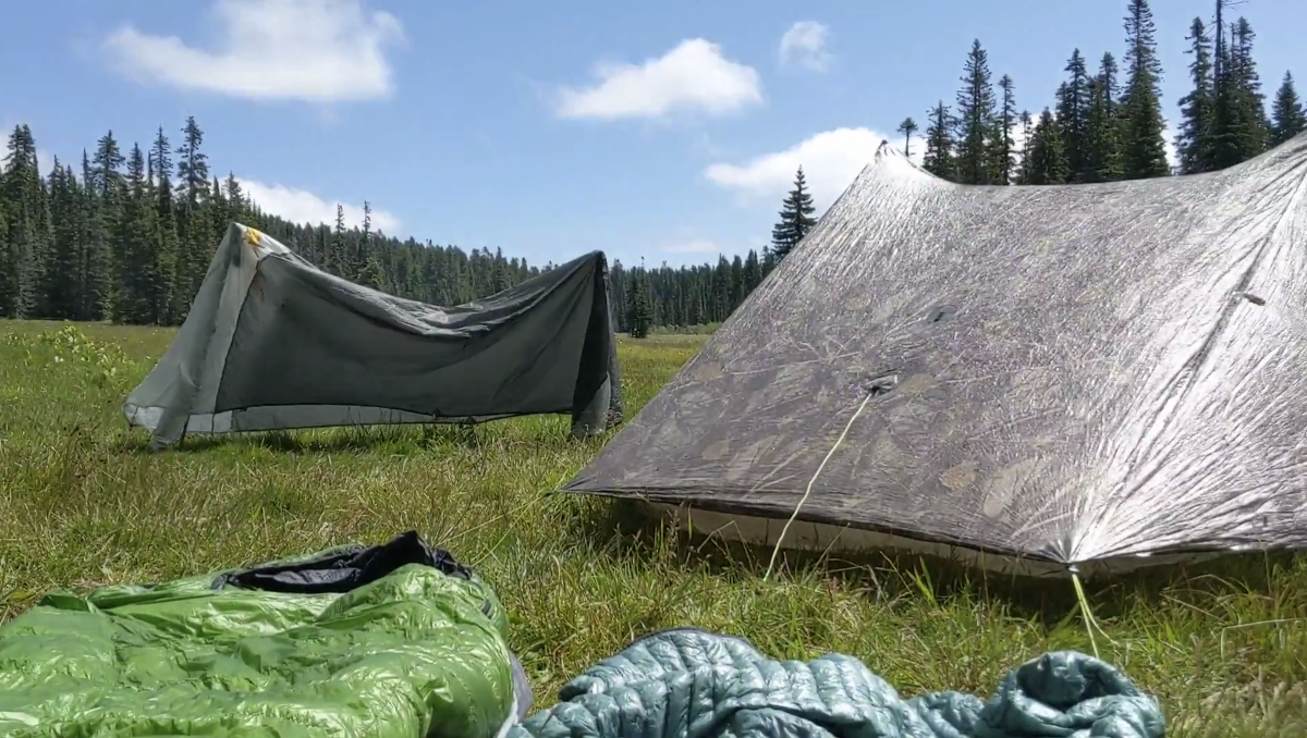 A rain fly drying on a pair of hiking poles, with a tent being dried after being set up under the sun. Photo by Tiffany Chou.