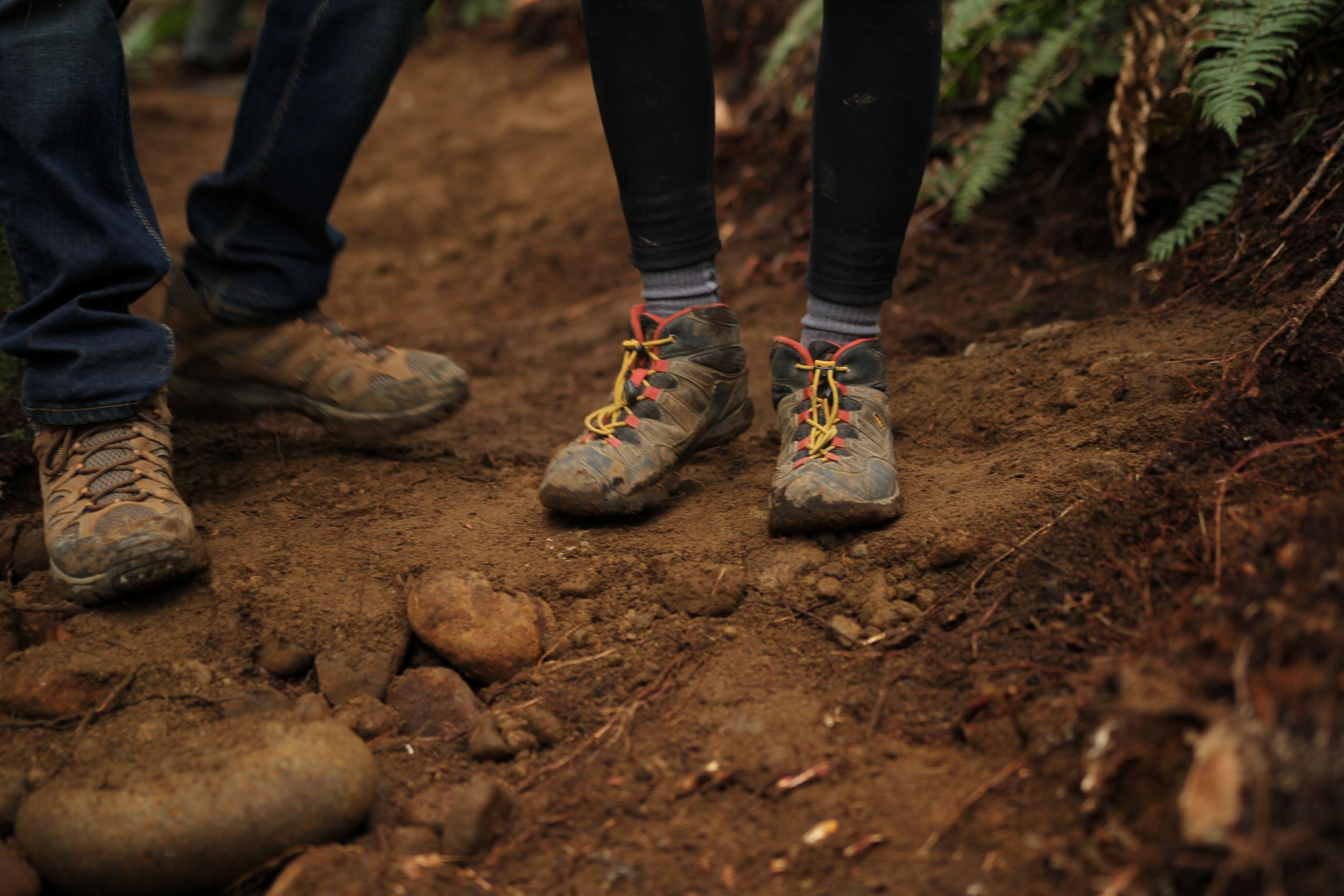 Mud is a pretty common sight on Washington's trails, so it's handy to have footwear that you don't getting a bit dirty. Two hikers in long pants and muddy boots stand on trail.
