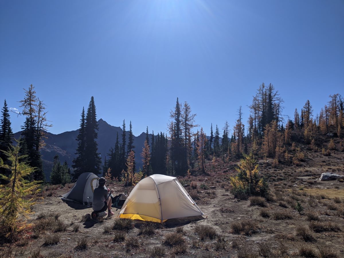 Hiker sitting on a sideways bear canister in the North Cascades. Photo by Tiffany Chou.