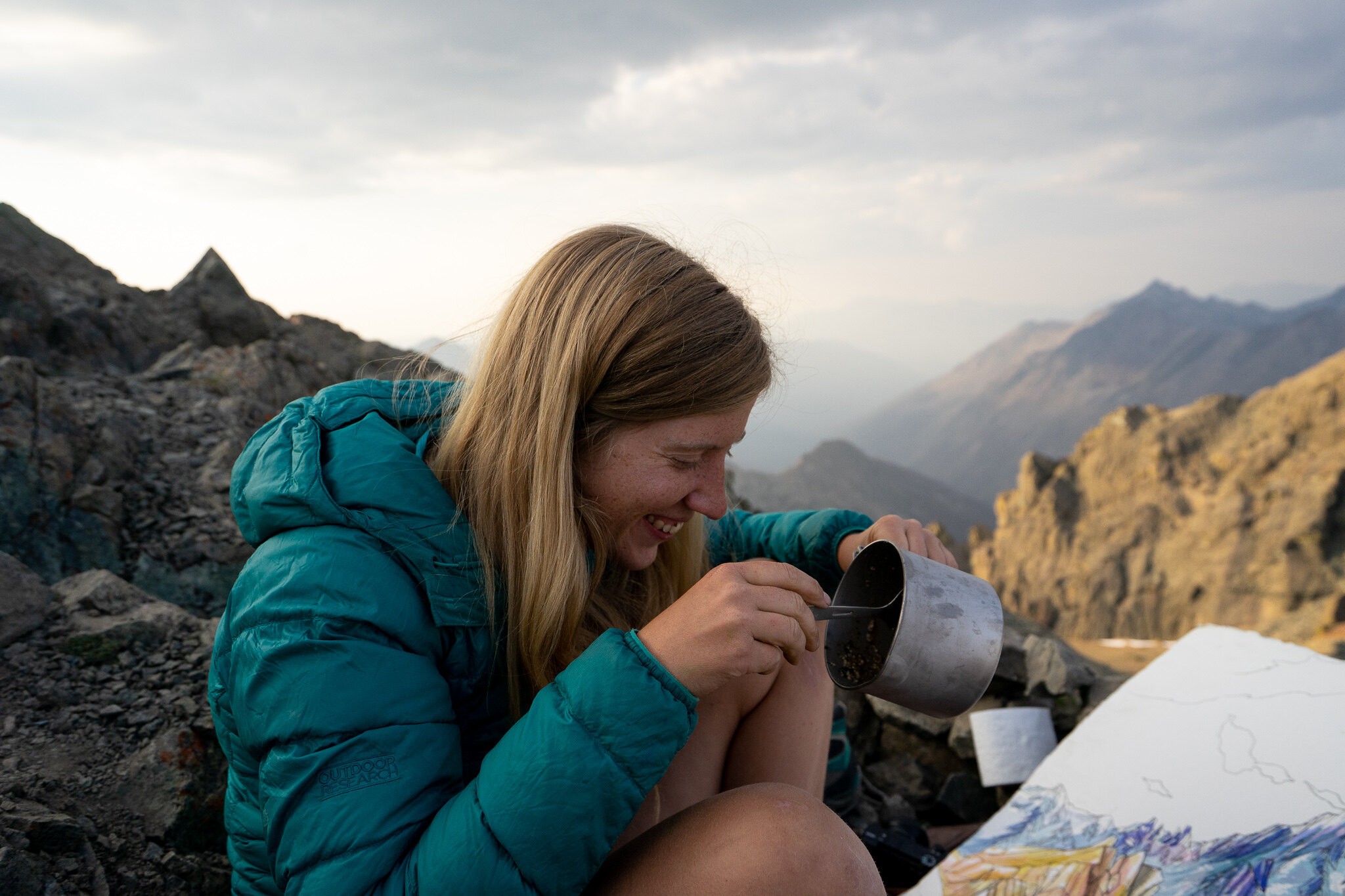 Hiker (Niki Frumkin - Drawn to High Places) making watercolor art while eating food out of a pot. Photo by Sarina Clark.