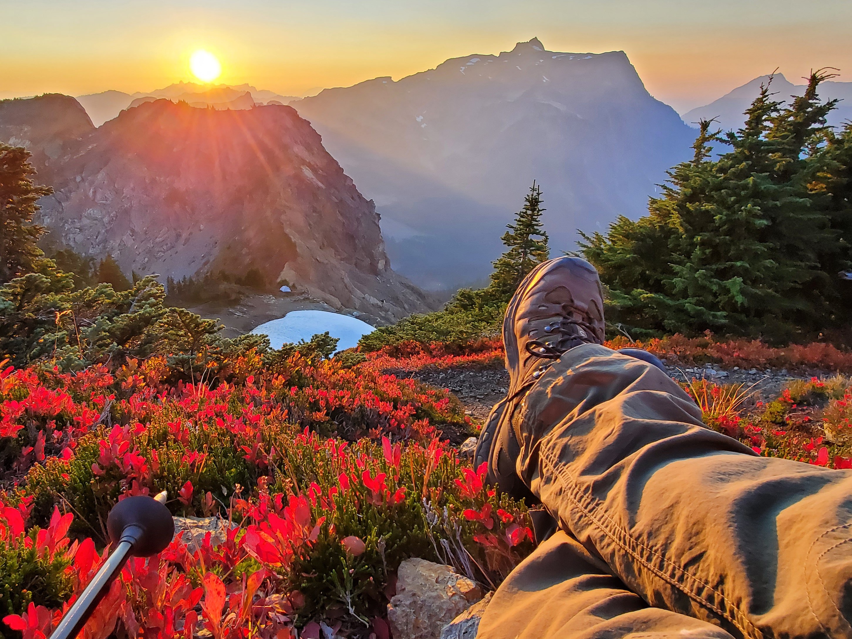 Boots are a durable choice of hiking footwear. A hiker sits with their boots out in front of them overlooking a sunset.