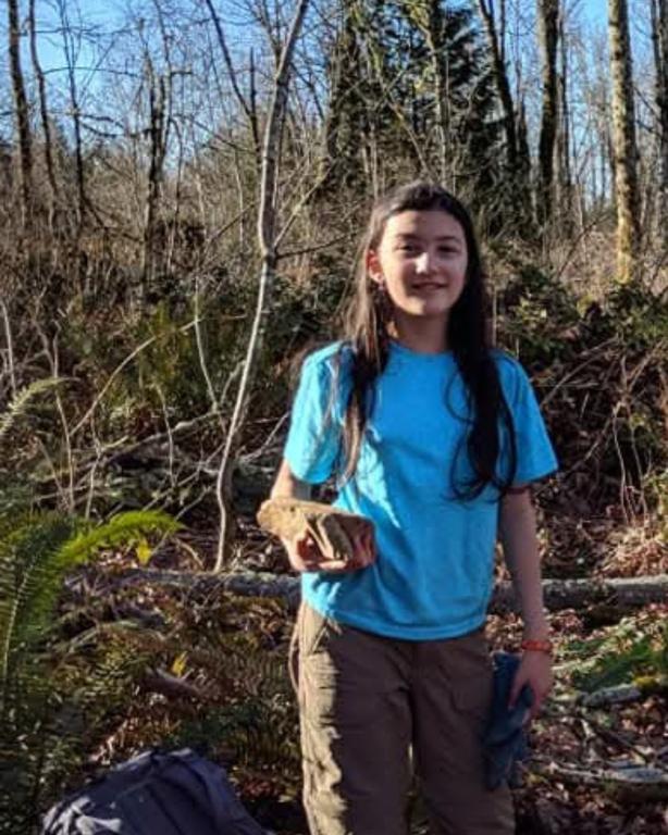 Youth on trail holding a rock outside at a WTA work party wearing a bright blue shirt.