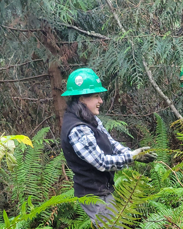 Volunteer on trail with black vest and green hard hat smiling and clapping.