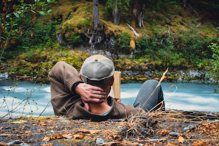 Hiker sitting by river reading a book
