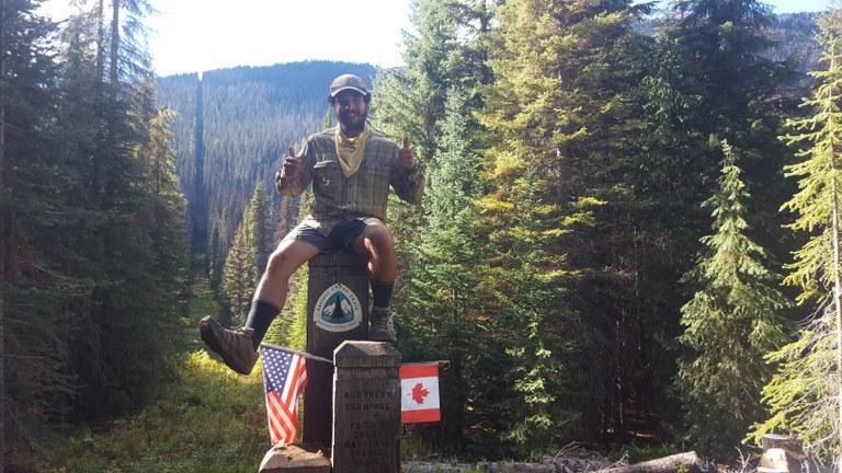 A hiker sits upon the old Northern Terminus for the PCT.
