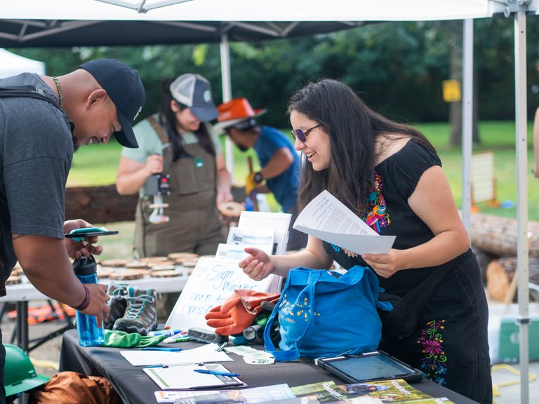 A festival attendee and facilitator chat over a booth.