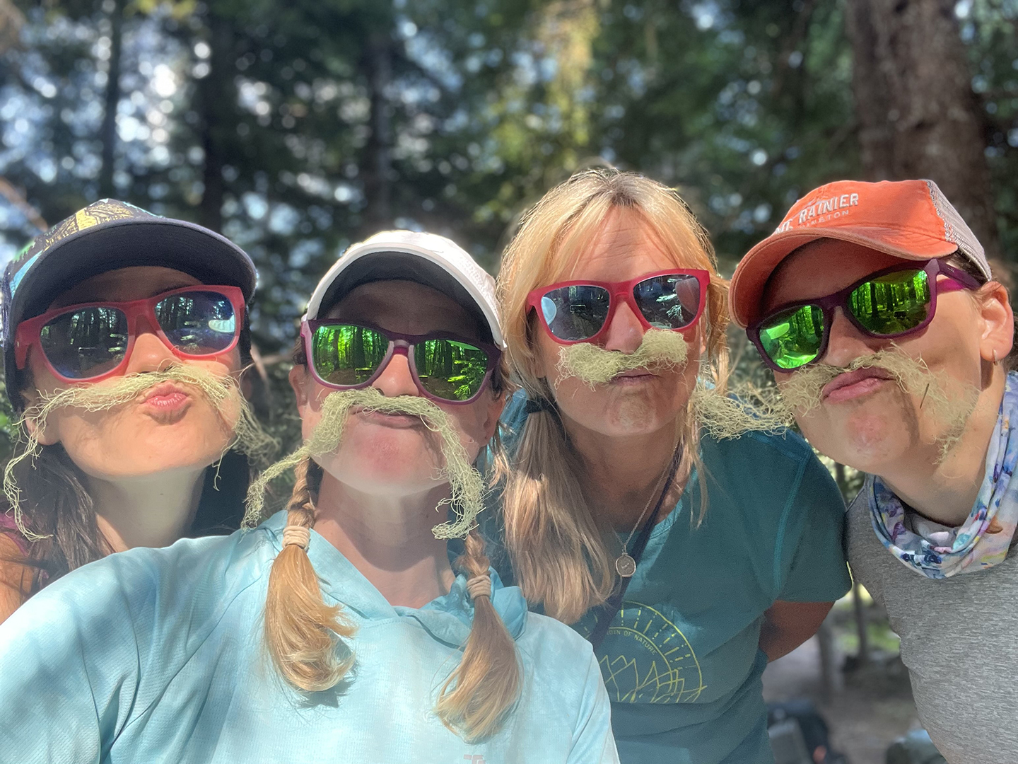 A group of hikers smiles at the camera, with moss mustaches. 