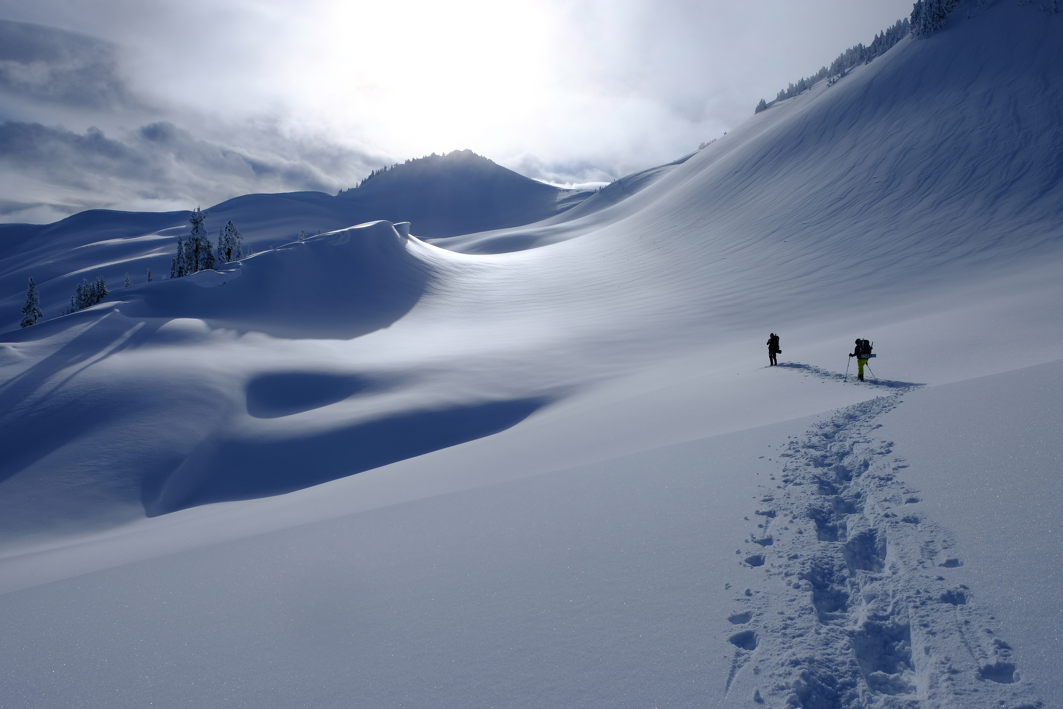 Snowshoers travese a smooth patch of snow among mountain peaks. 