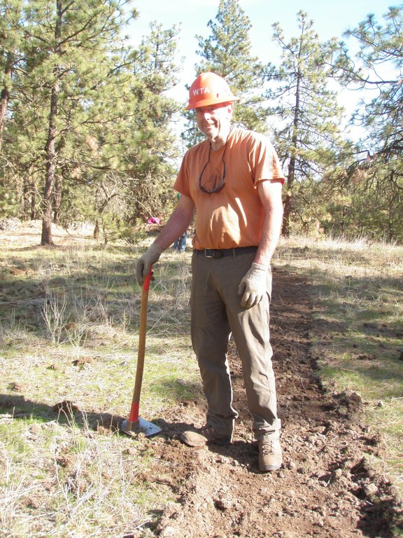 Alan stands on trail with a grub hoe in one hand.