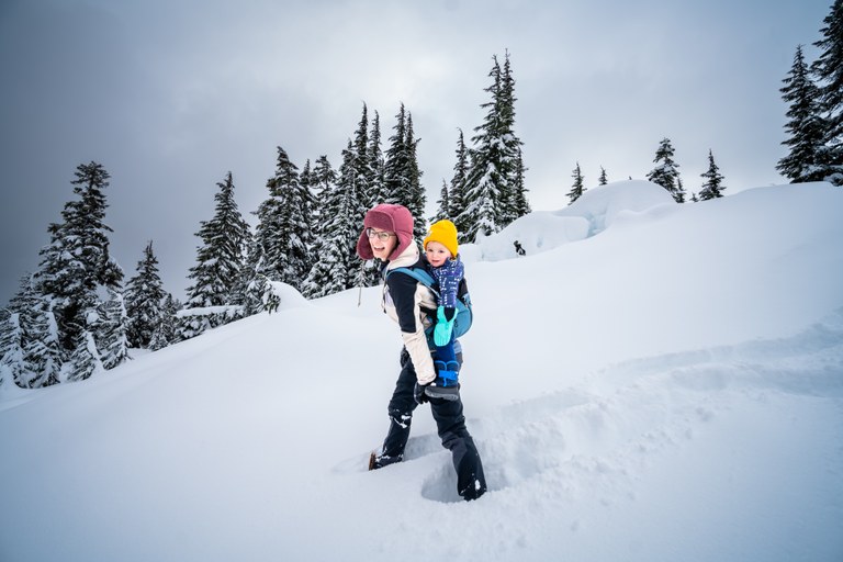Artist Point. Photo by Kevin Rabuck. A parent in the snow with a young child in a carrier on their back.