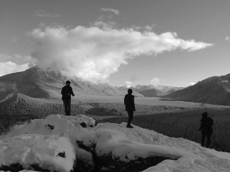 Hikers appreciate the winter landscape from a snowy outcrop.
