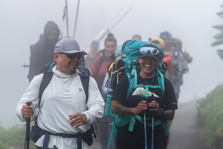 Rachel and the all-Native team smile with backpacks on as they walk on a misty trail.