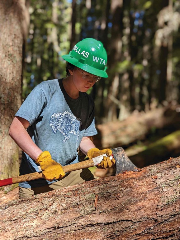 Dallas using an axe to debark a large log. Photo by Zachary Toliver.
