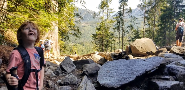 A young child looks up smiling while standing on a trail.